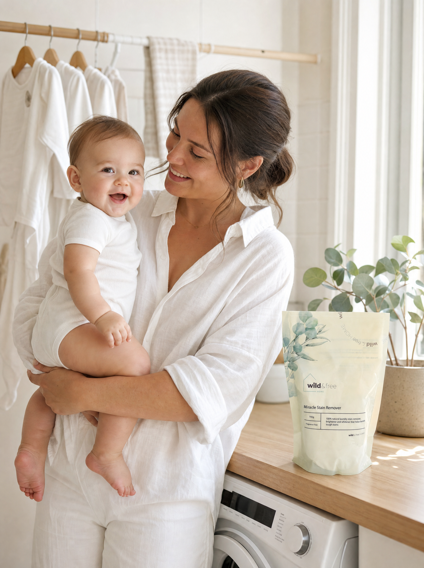 Mum holding baby in laundry room next to Wild & Free Home Miracle Stain Remover